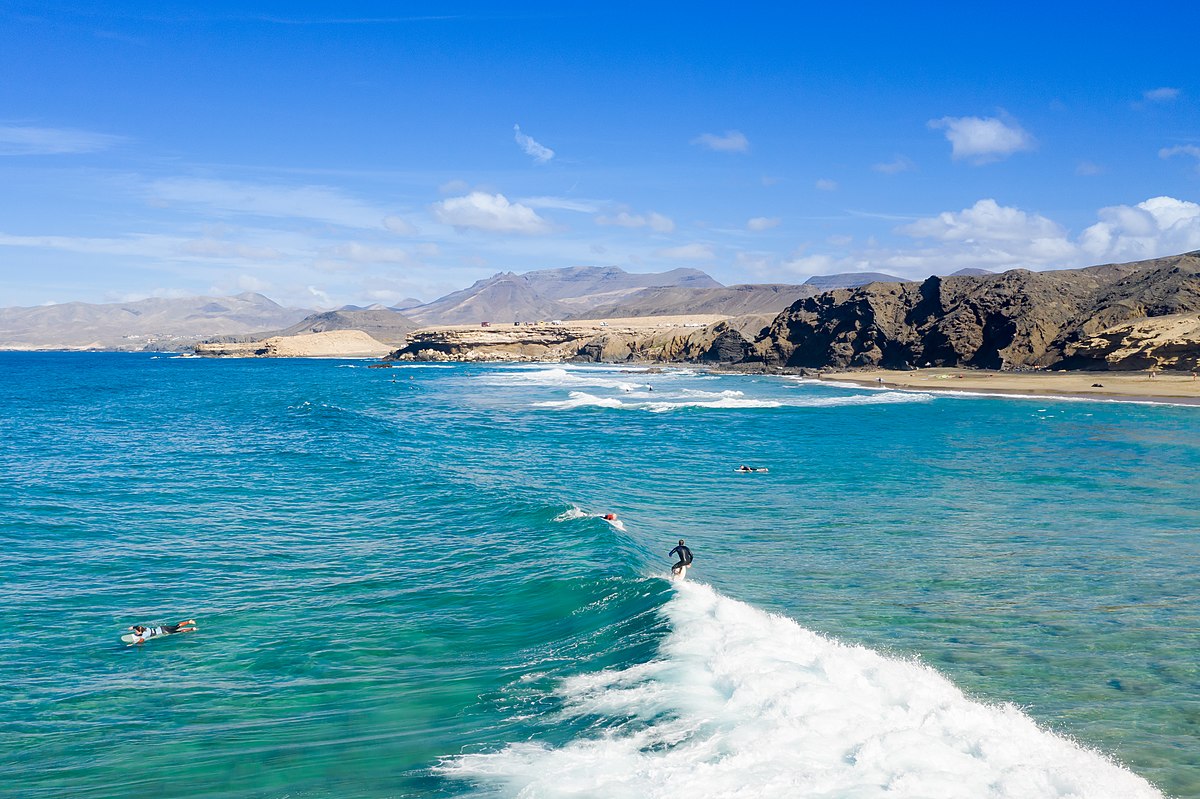 Sunny and windy: perfect surfing conditions in Fuerteventura Surfer riding Atlantic waves in Fuerteventura under bright sun