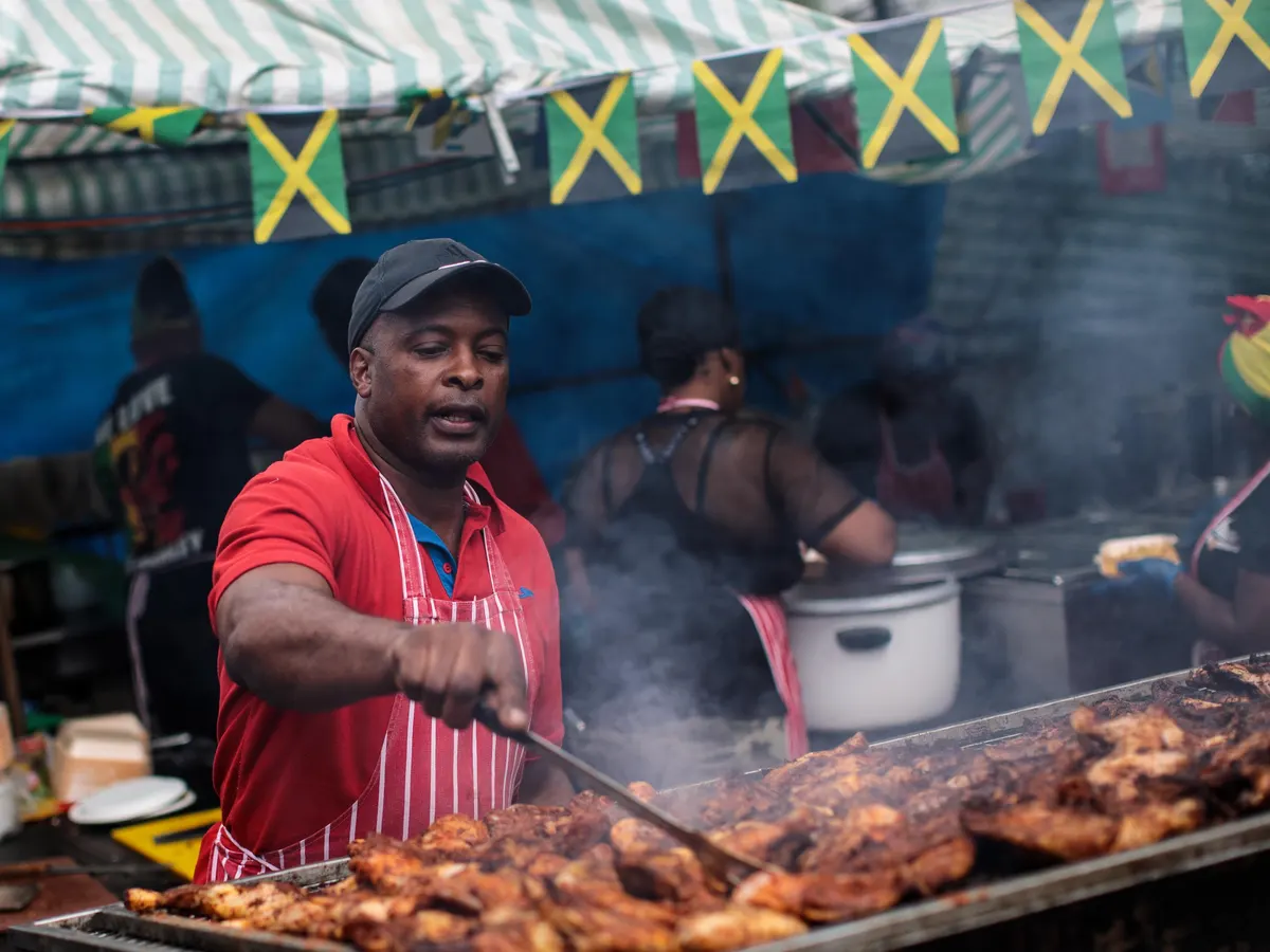 Food & Drinks in Jamaica – Jerk Street Food & Local Flavors Jamaican jerk chicken being grilled at a local street food stall, representing Jamaica’s food and drink culture