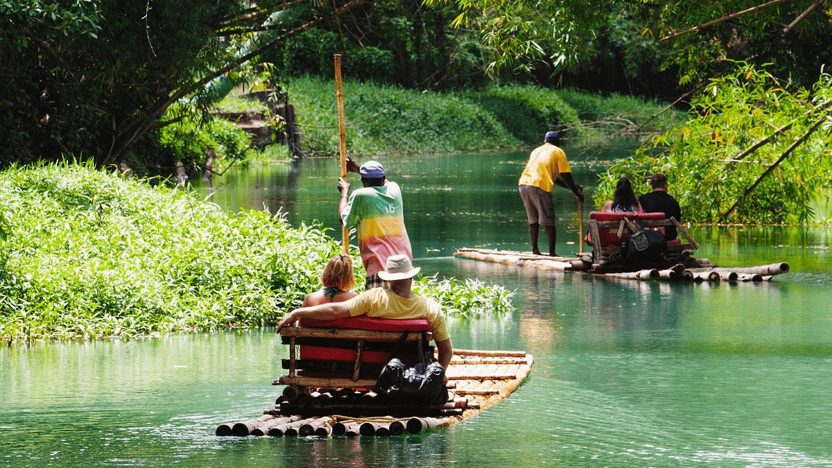 Bamboo Rafting in Jamaica – A Relaxing River Experience Travelers enjoying a bamboo rafting experience on a calm river in Jamaica surrounded by lush rainforest