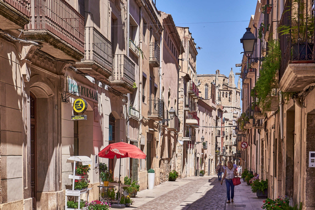 Spain Travel Tips – Everyday Spanish lifestyle and Mediterranean street scenes A charming Spanish street with traditional Mediterranean architecture, local shops and people strolling on a sunny afternoon